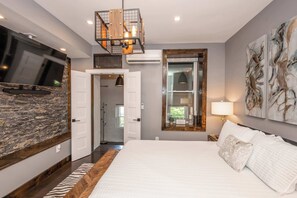 Een slaapkamer met een groot bed, een wandgemonteerde televisie, een accentmuur van steen, een vloerkleed van hout en een groot raam met uitzicht.
