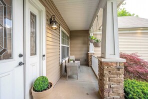 A covered porch with a stone column, a potted plant, and a wicker chair.