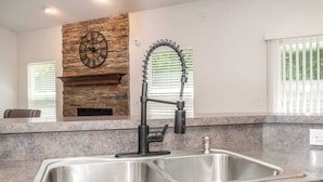 A kitchen with granite countertops, a stainless steel sink, a stone fireplace, and a clock on the wall. - Urban Escape (Cincinnati)