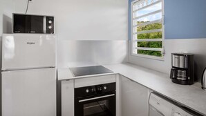 A compact kitchen with a microwave, oven, dishwasher, and a coffee maker. - Apartment Alizés - Sea view & Direct beach access (Le quartier le Coin)