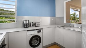 A compact kitchen with a washing machine, a coffee maker, and a toaster. - Apartment Alizés - Sea view & Direct beach access (Le quartier le Coin)