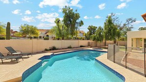 A rectangular swimming pool with blue tiles, surrounded by lounge chairs and a fence.