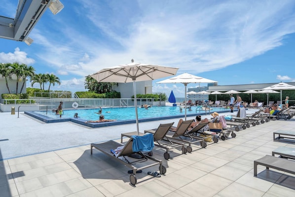 A rooftop pool area with lounge chairs, umbrellas, and a swimming pool.