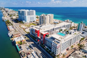 An aerial view of a coastal hotel area with multiple high-rise buildings, a marina, and a clear view of the ocean.