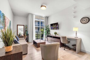 A modern living room with a sofa, a desk, and a large window offering a view of a building. - BEACHFRONT CONDO WITH ROOFTOP POOL (Hollywood)