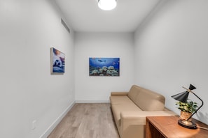 A modern living room with a beige sofa, a wooden coffee table, and a black floor lamp. There are two framed pictures on the wall, one depicting a car and the other an underwater scene. - BEACHFRONT CONDO WITH ROOFTOP POOL (Hollywood)