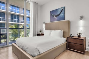 A modern hotel room with a large bed, a nightstand with a phone and a plant, a wall-mounted light, and a painting of a whale.