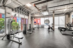 A gym with various exercise equipment, large windows, and a concrete ceiling. - BEACHFRONT CONDO WITH ROOFTOP POOL (Hollywood)