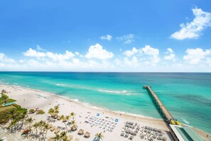 A beach with a pier extending into the ocean, rows of beach chairs, and umbrellas.