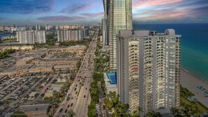 A high-rise building with a curved facade, adjacent to a beachfront and a parking lot. - A Breathtaking Oceanview – High Rise Luxury Condo! (SUNNY ISLES BEACH)