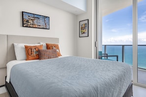 A bedroom with a large bed, a view of the ocean, and artwork on the walls.