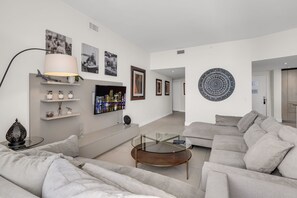 A modern living room with a sofa, a glass coffee table, and a TV mounted on the wall. - Stunning  Penthouse  Resort Amenities  12 people (Hollywood)