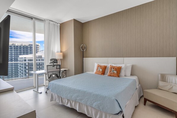 Una habitación de hotel moderna con una cama grande, un escritorio y vistas de la ciudad a través de ventanales.