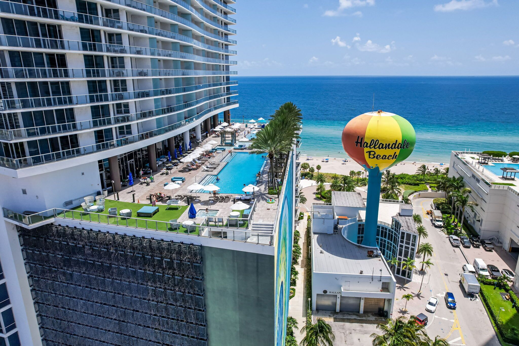 A hotel with a pool, beach, and a large sign for Hallandale Beach.