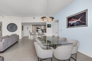 A modern living room with a glass-top dining table, grey sofas, and a kitchen in the background. - LYFE Resort | 39th Floor Oceanview Penthouse (Hollywood)