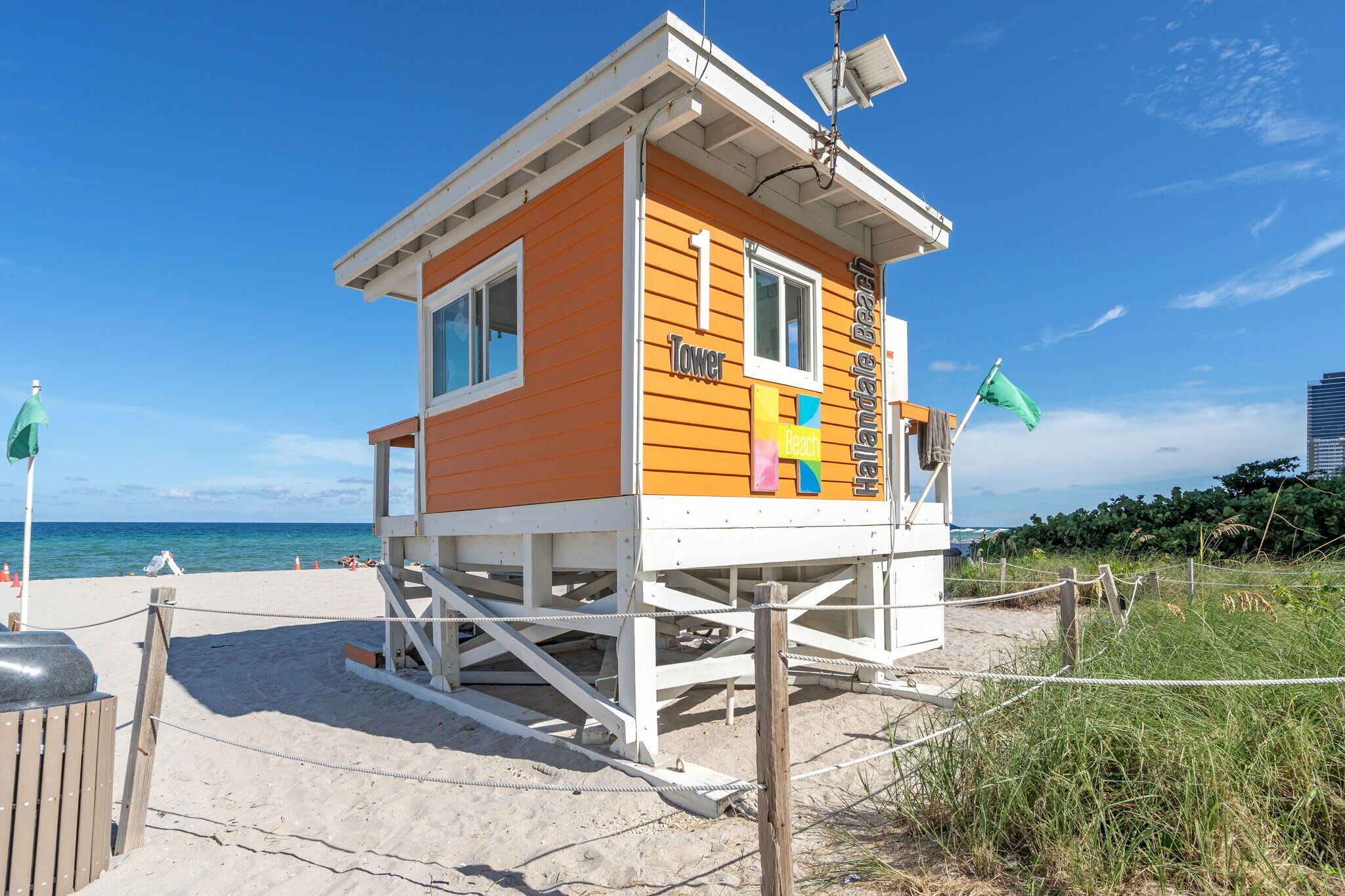 A beach lifeguard tower with a sign indicating 'Tower' and 'Beach' on the side, situated on a sandy beach with a clear sky.