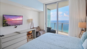 Habitación de hotel con cama, escritorio, silla, televisión y balcón con vista al mar.
