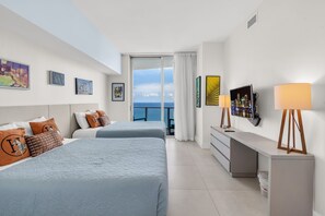 Habitación de hotel con dos camas, un escritorio, un televisor y un balcón con vistas a la ciudad.