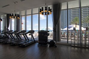 A gym with treadmills, a rowing machine, and a kettlebell rack. Large windows offer views of a pool and a high-rise building.