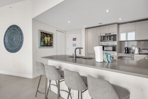 A modern kitchen with a central island, bar stools, and a microwave. - LYFE Resort | 39th Floor Oceanview Penthouse (Hollywood)