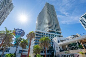 A modern hotel with a curved facade, palm trees, and a sign for 'Hollandale Beach'. - LYFE Resort | 39th Floor Oceanview Penthouse (Hollywood)