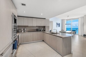 A modern kitchen with a large island, built-in appliances, and a view of the ocean.