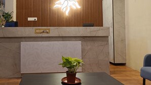 Zona de recepción con pared de paneles de madera, mostrador de recepción, planta en maceta y pared de mármol.