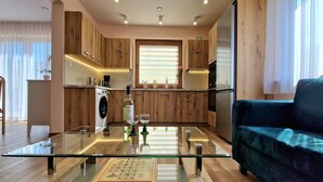 A modern kitchen with wooden cabinets, a glass-top dining table, and a sofa in the living area. - Holiday Home Wiśniowa with Pool and Mountains (Iwierzyce)