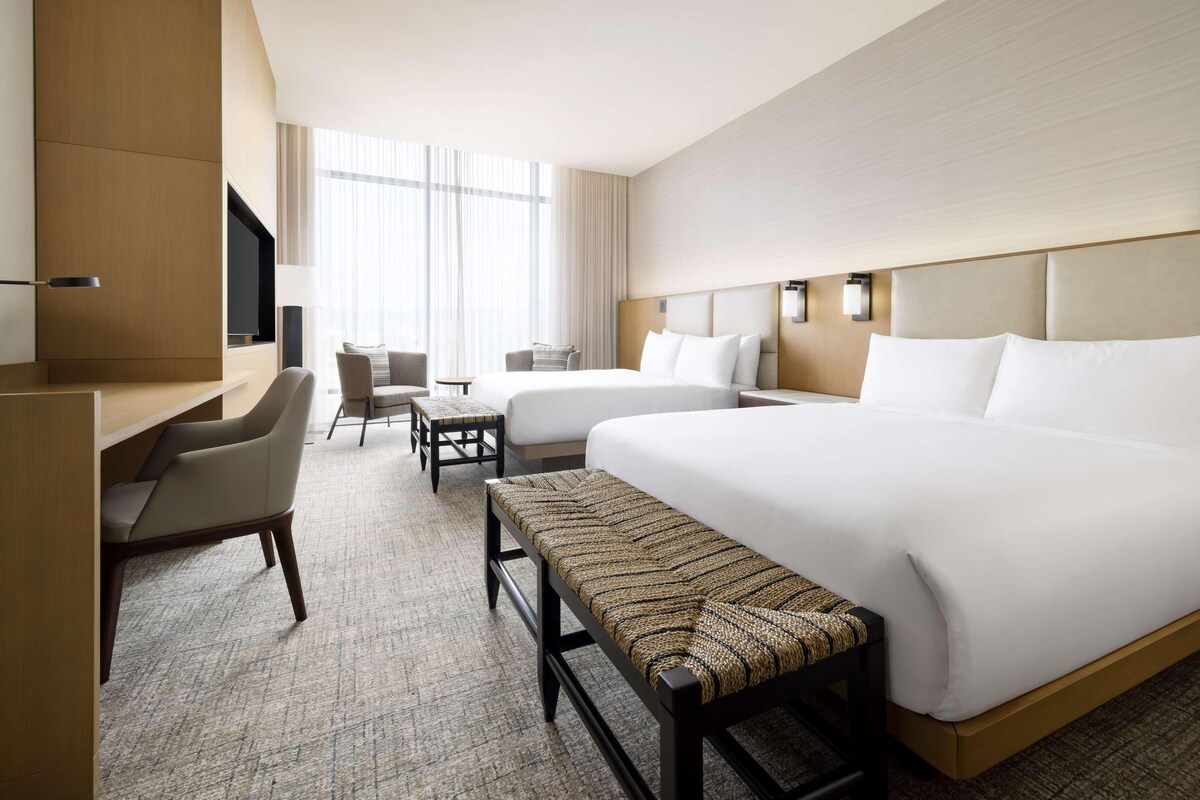 A hotel room with a large bed, a desk, a chair, a bench, and a television.