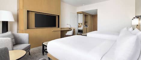 A modern hotel room with a large bed, a sofa, a small table, a TV mounted on the wall, and a mirror.