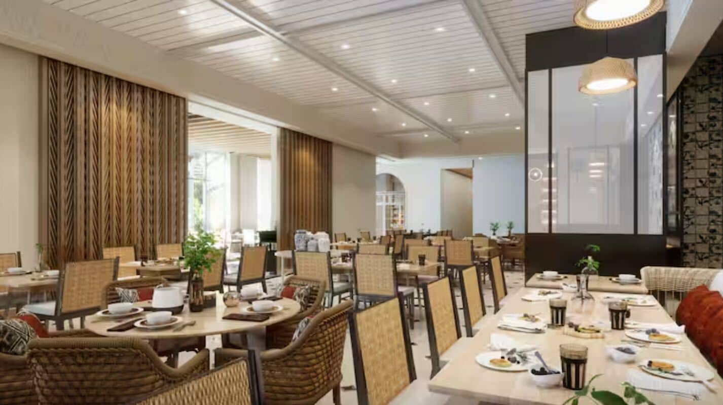 A spacious dining area with multiple tables and chairs, large windows, and a modern ceiling design.