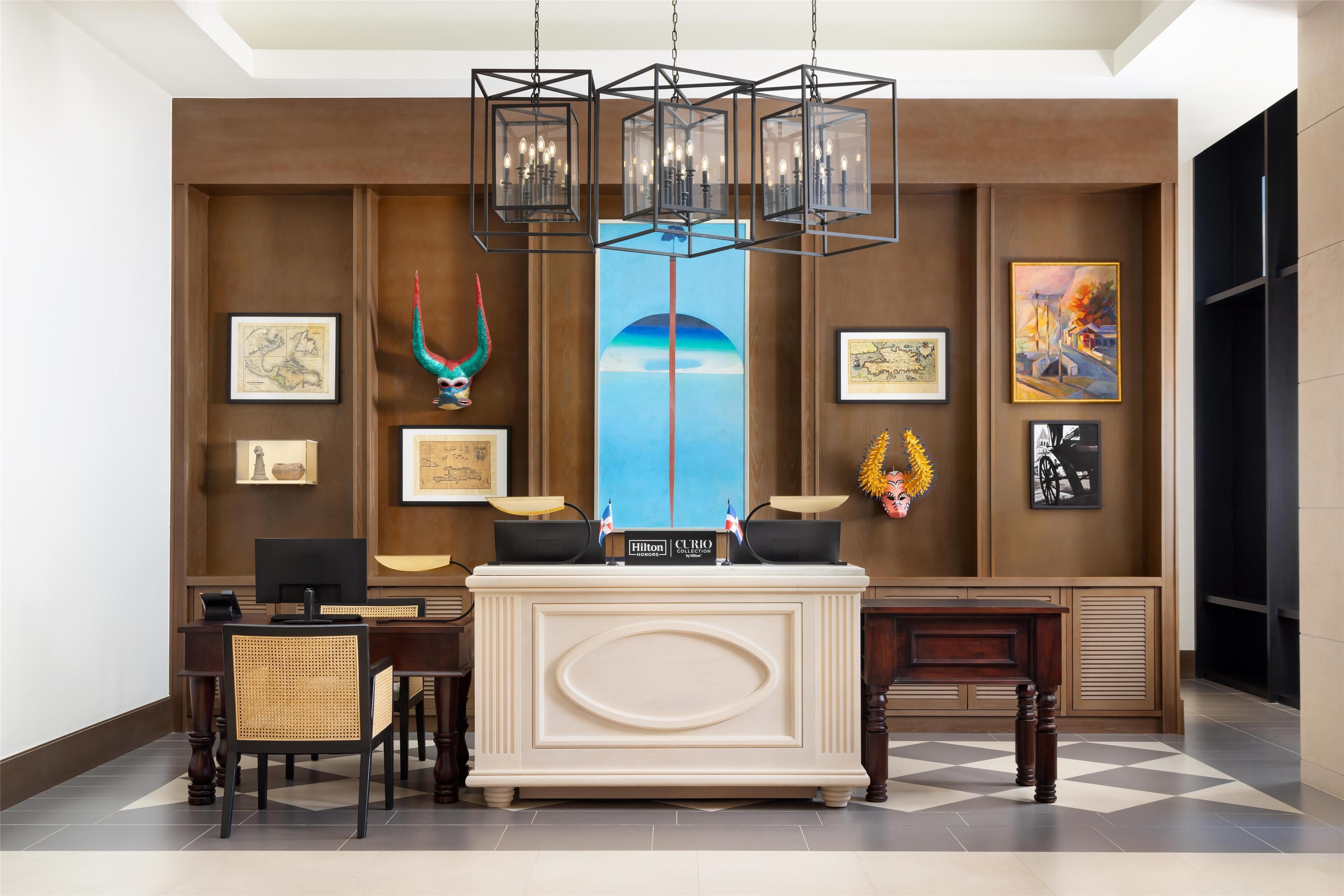 A hotel reception area with a reception desk, chairs, a large painting, and a chandelier.