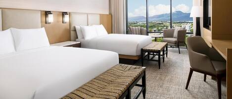 A hotel room with two beds, a desk, a chair, a bench, and a large window offering a city view.