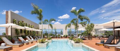 A pool area with lounge chairs, umbrellas, and palm trees.