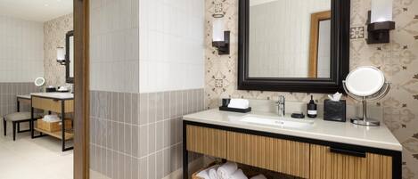 Un baño con un espejo grande, un lavabo, una tocador y una cesta de mimbre debajo del mostrador.