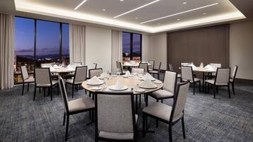 A conference room with round tables set for dining, large windows with curtains, and a carpeted floor.