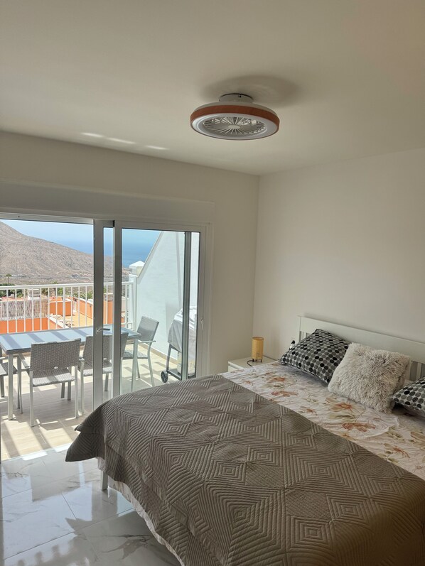 Ein Schlafzimmer mit Bett, Nachttisch, Lampe und Blick ins Freie.