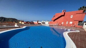 Ein Schwimmbecken mit zwei Leitern, umgeben von einer gefliesten Terrasse, und ein rotes Gebäude im Hintergrund.
