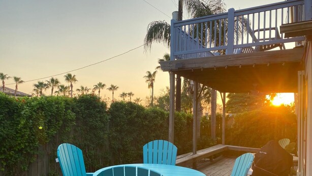 A wooden deck with a round table and four chairs, overlooking a garden with palm trees.