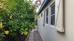 A narrow pathway leading to a building with a white exterior and a window with a white frame.