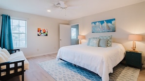 A bedroom with a bed, a nightstand, a chair, a ceiling fan, and artwork on the walls.
