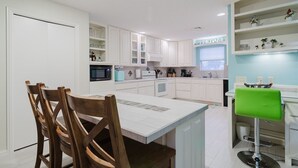 A modern kitchen with white cabinets, a central island, and a green bar stool.