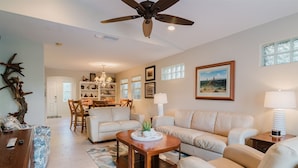 A spacious living room with a high ceiling fan, a dining area with a chandelier, and a kitchen in the background.