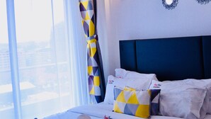 A hotel room with a large bed, a view of the city, a patterned curtain, and decorative wall mirrors. - spacious 3 bedroom in kilimani gym&pool (Nairobi)
