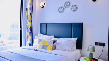 A hotel room with a bed, a round side table with a lamp, and decorative wall mirrors.