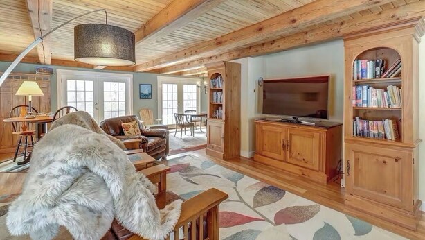 A spacious living room with wooden beams, a large TV, and a bookshelf. - Charming 3-bedroom house in marvelous Moretown (Moretown)