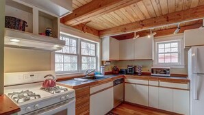 A kitchen with wooden beams, white cabinets, a stove, a sink, and a refrigerator. - Charming 3-bedroom house in marvelous Moretown (Moretown)