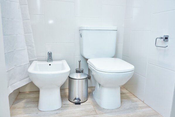 Une salle de bain équipée d’un bidet, de toilettes et d’une poubelle.