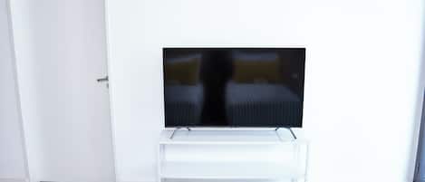 A room with a television on a white stand, a door, and two striped beds.