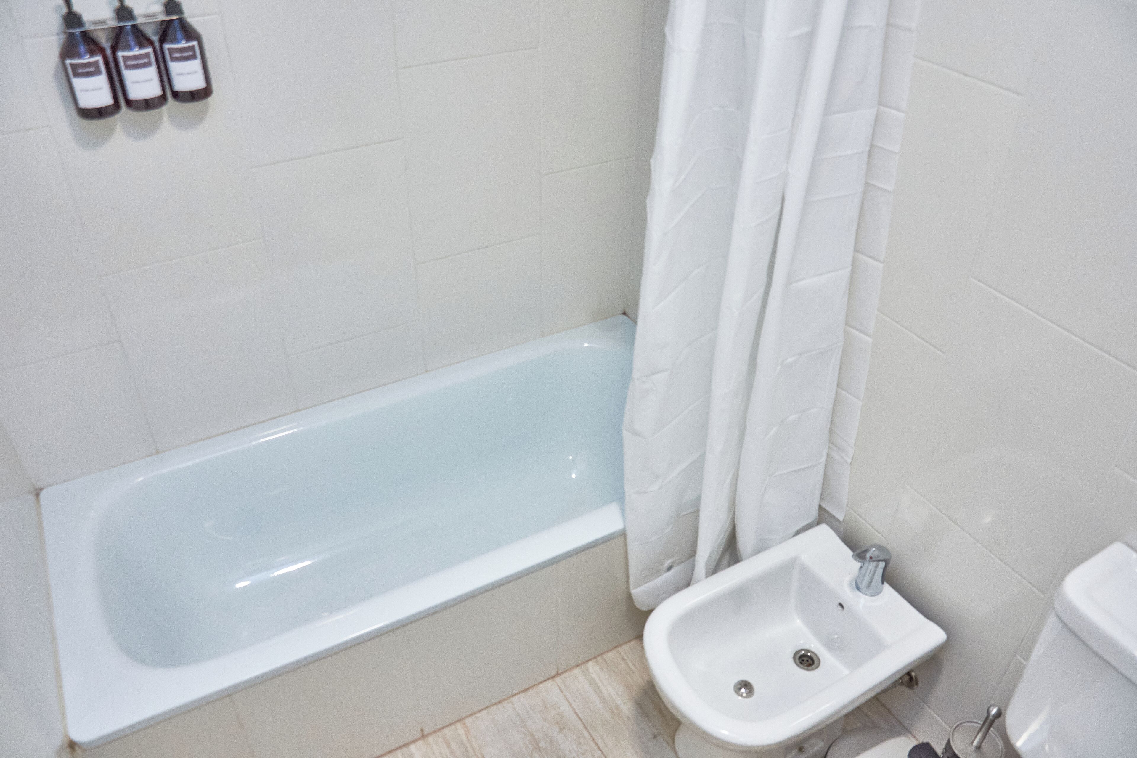 A bathroom with a bathtub, a sink, and a toilet. There are three bottles on the wall above the bathtub.
